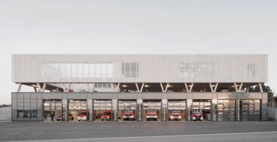 Feuerwehrhaus Straubenhardt mit beleuchteter Fahrzeughalle, moderne Betonarchitektur mit V-förmigen Stützen und durchgehender Glasfassade, rote Feuerwehrfahrzeuge sichtbar